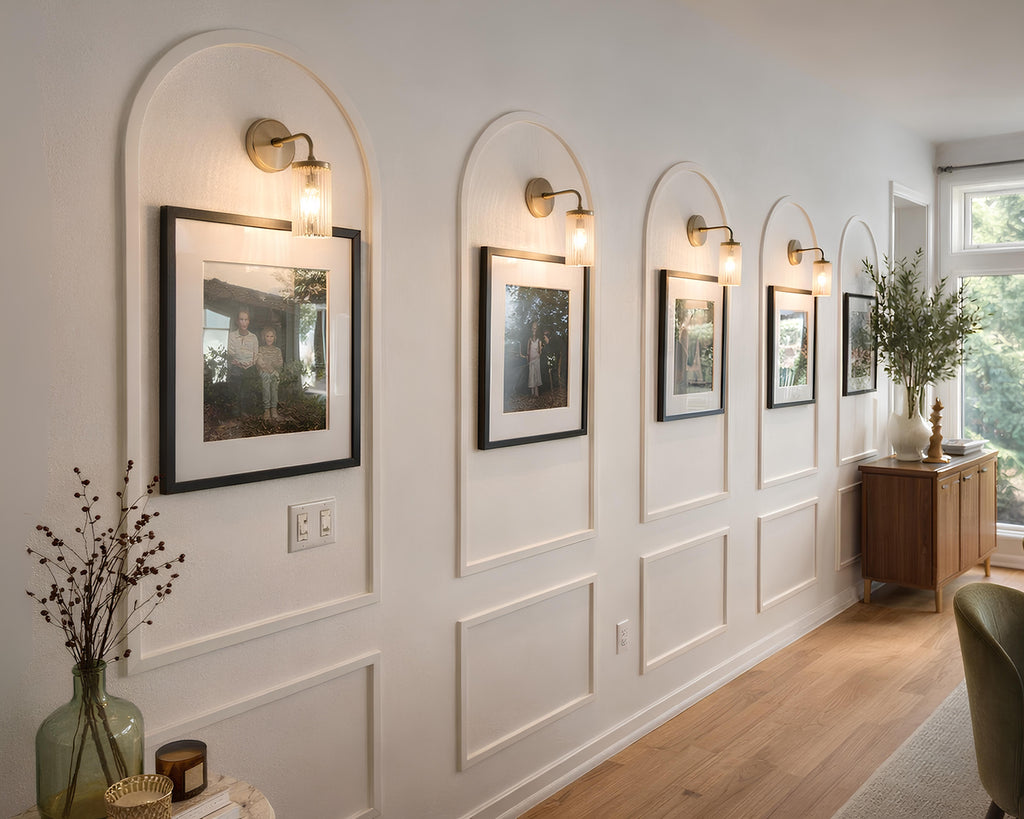 Decorative wall with arched wall molding, framed landscape pictures, wall sconces, and a wooden console table.