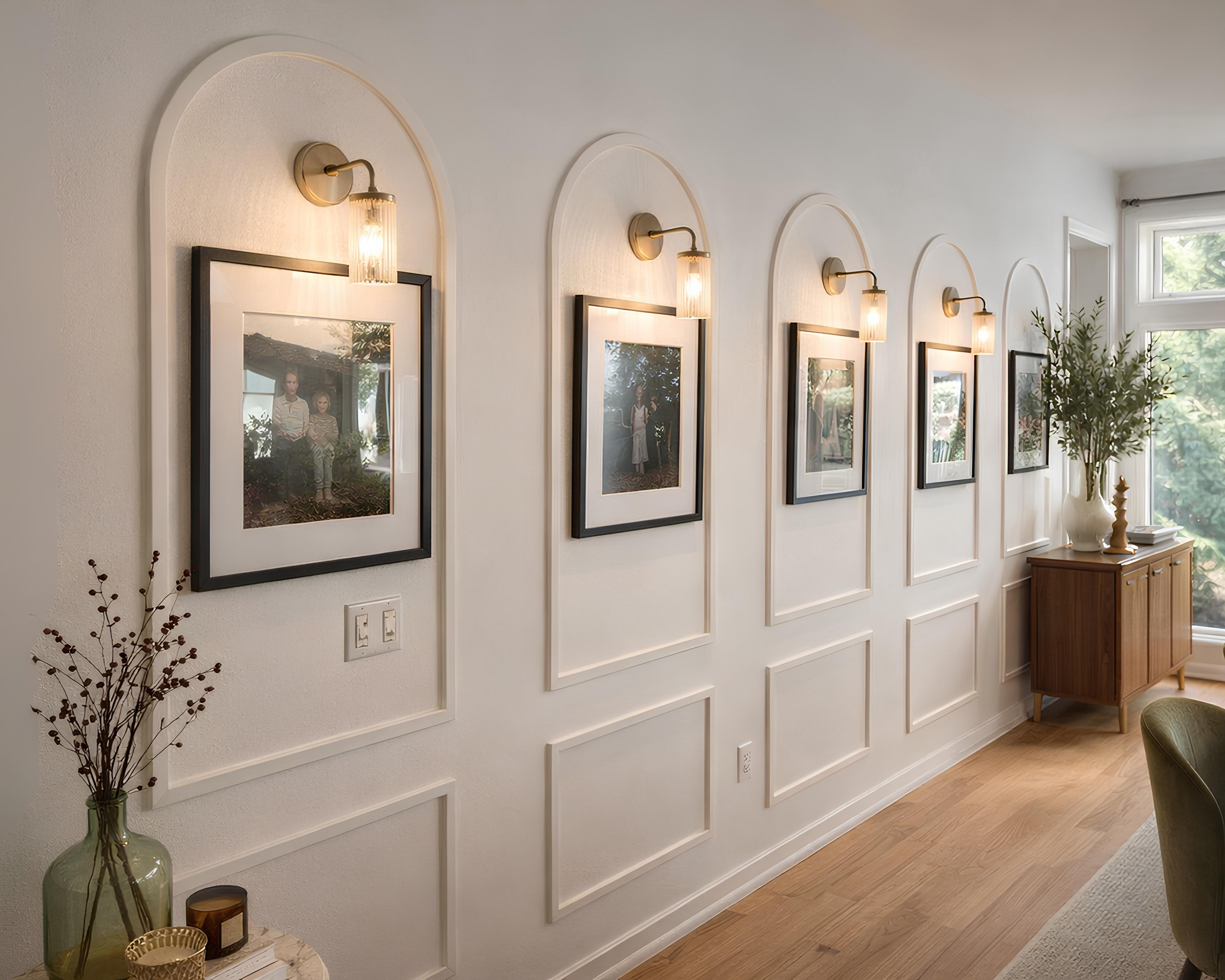 Decorative wall with arched wall molding, framed landscape pictures, wall sconces, and a wooden console table.