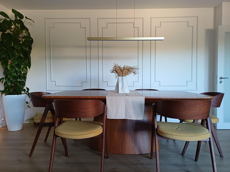 decorative wall molding panels creating elegant dining room accent wall-Dining room with wooden table and chairs with yellow cushions, white walls, and a plant.