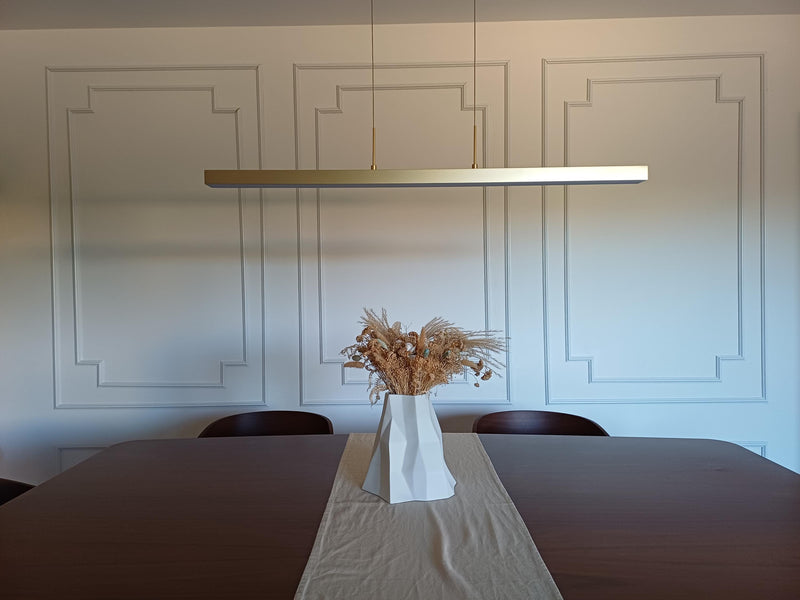 decorative wall molding panels creating elegant dining room accent wall-Modern dining room with a long table, vase of dried flowers, and a linear pendant light.