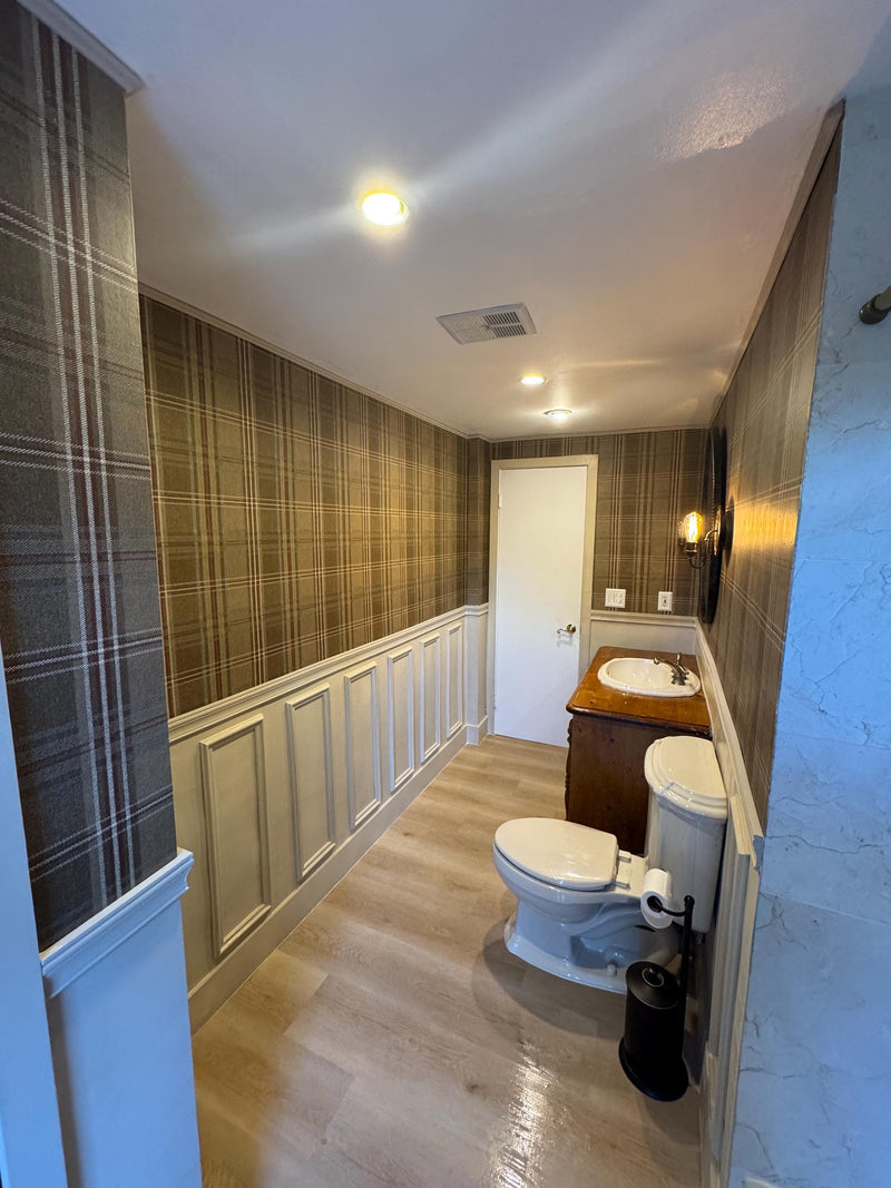 DIY half of wall molding panel design completed in modern bathroom with wooden vanity, toilet, and sink against a plaid wall.