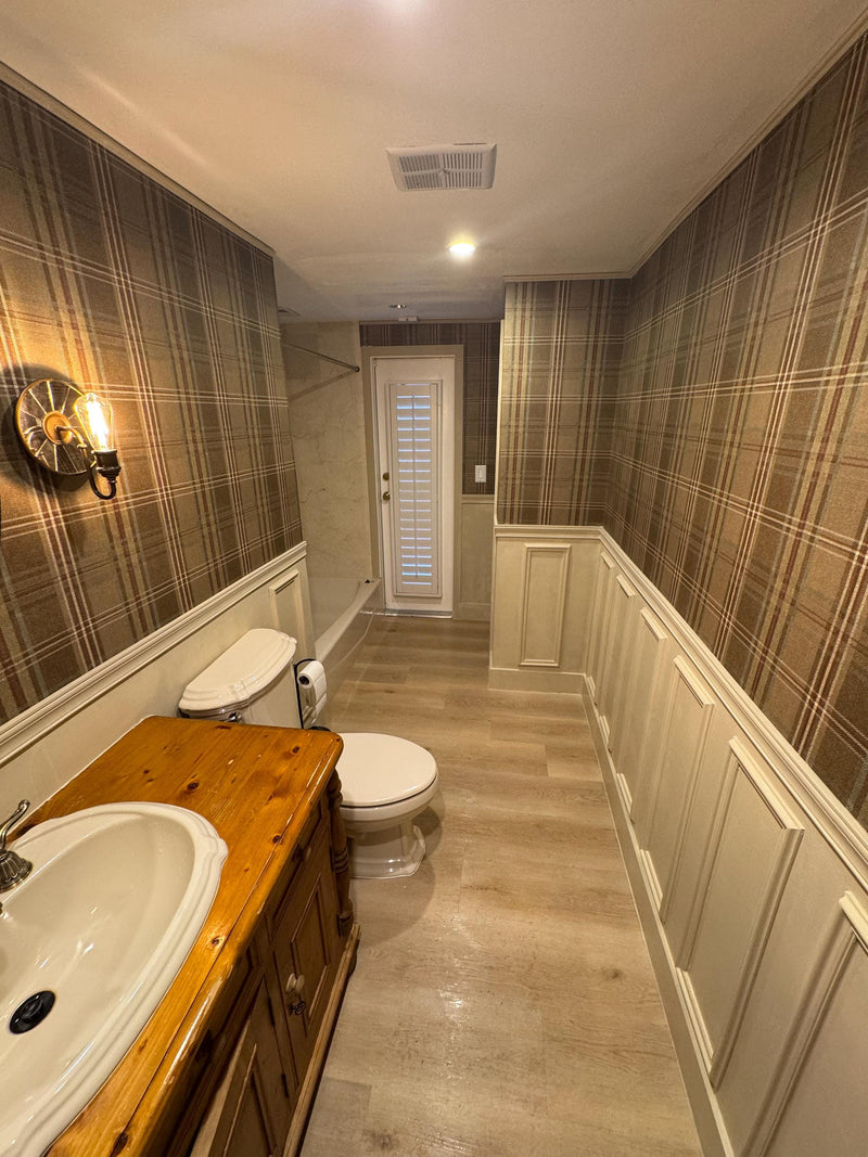 DIY half of wall molding panel design completed in modern bathroom with plaid walls, wooden vanity, and white toilet.