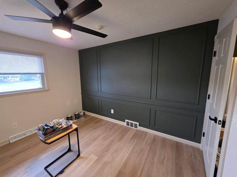 DIY picture frame wall molding panel design completed in modern living room-Room interior with dark paneled wall, ceiling fan, and small table.