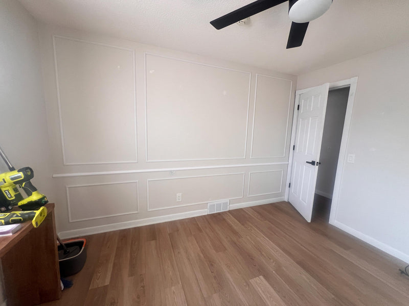 DIY picture frame wall molding panel design completed in modern living room-Room with white paneled walls and wooden flooring, showing construction or renovation work.