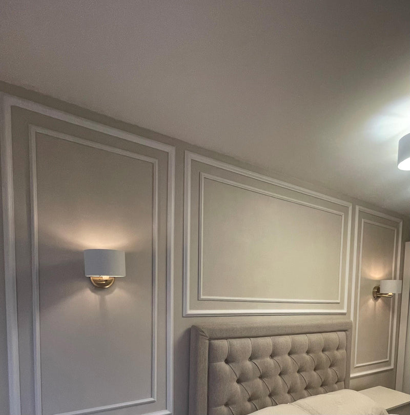 Neatly decorated bedroom with panelled walls, a tufted headboard, and wall lights.