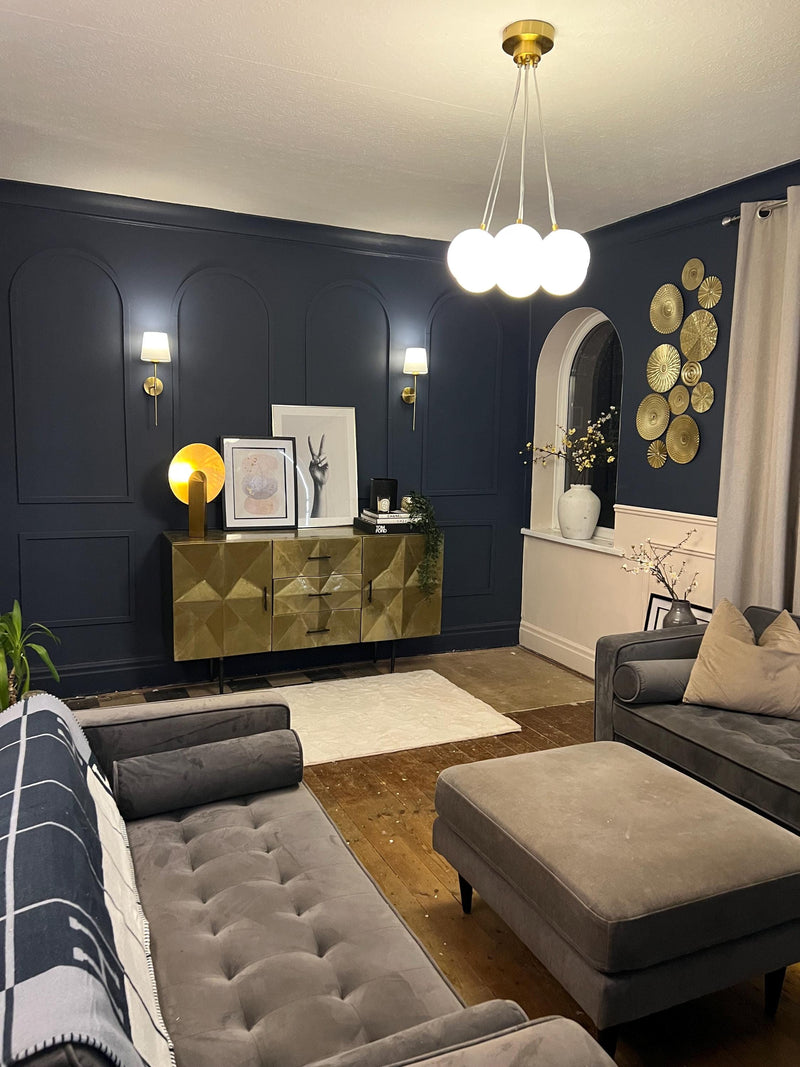 real home accent wall created with DIY wall molding trim kit-Modern living room with dark blue walls, gray sofa, and gold accents.